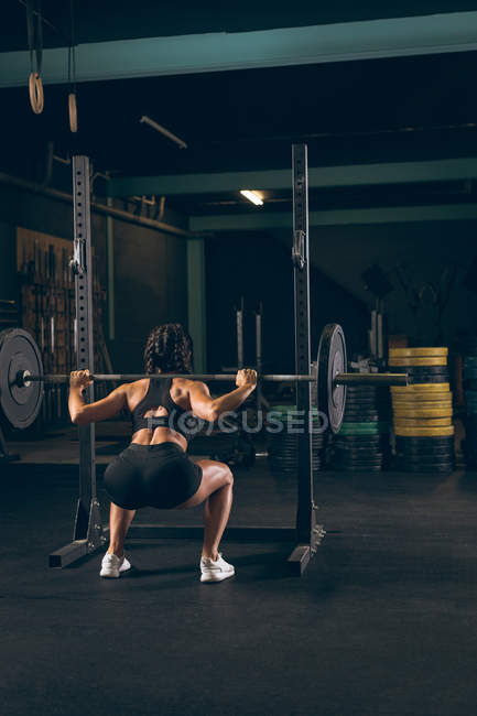 Visão traseira da mulher em forma levantando a barra no ginásio — Fotografia de Stock
