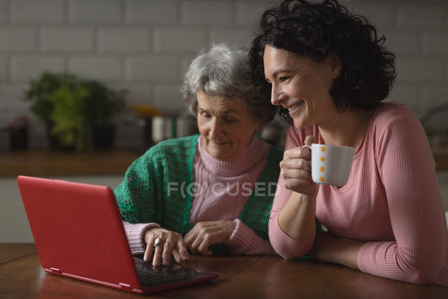 Mère et fille utilisant un ordinateur portable dans la cuisine à la maison — Photo de stock