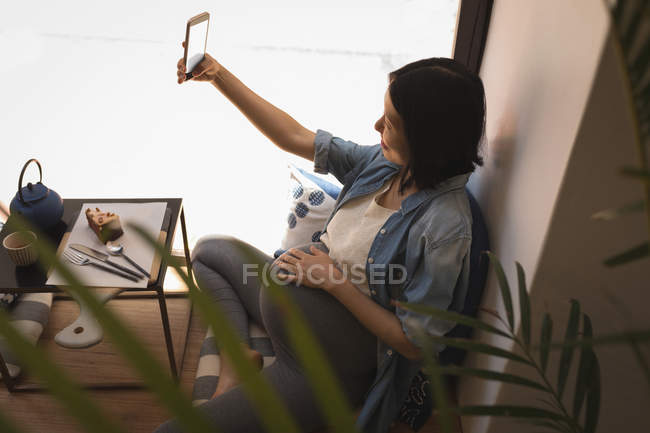 Вагітна жінка говорить селфі з мобільним телефоном у кафе — стокове фото