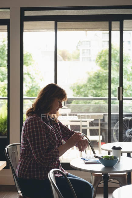 Mujer de negocios usando smartwatch en cafetería en la oficina - foto de stock