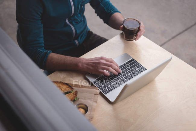 Sección media del hombre usando el ordenador portátil en la cafetería - foto de stock