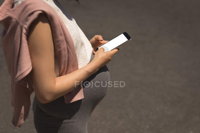 Беременная женщина пользуется мобильным телефоном в солнечный день — стоковое фото