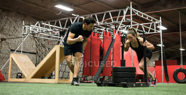 Тренер помогает женщине с санями толкая в фитнес-студии — стоковое фото