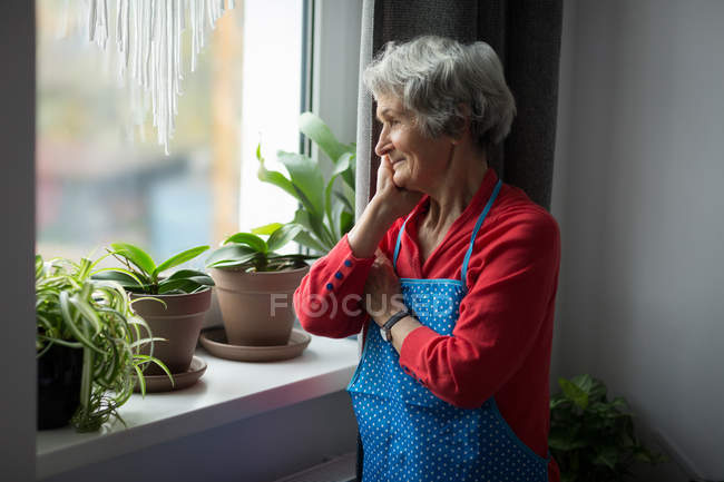 Nachdenkliche Seniorin schaut zu Hause durch Fenster — Stockfoto