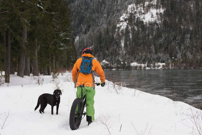 Man with bicycle looking at dog on a snowy landscape during winter — Stock Photo