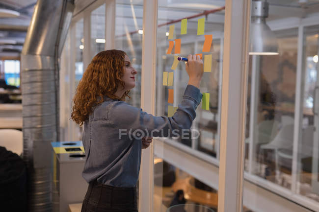 Female executive writing on sticky note in office — Stock Photo