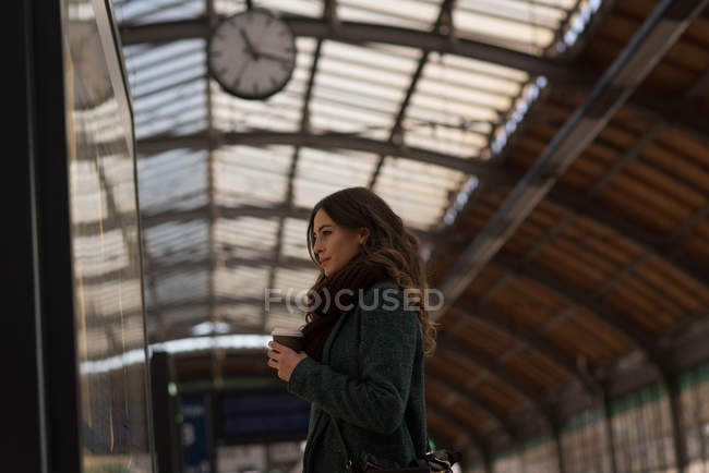 Задумчивая женщина пьет кофе на вокзале — стоковое фото