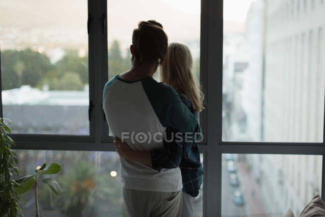 Coppia che si abbraccia vicino alla finestra di casa — Foto stock