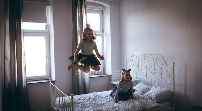 Sisters in costume playing on bed in bedroom — Stock Photo