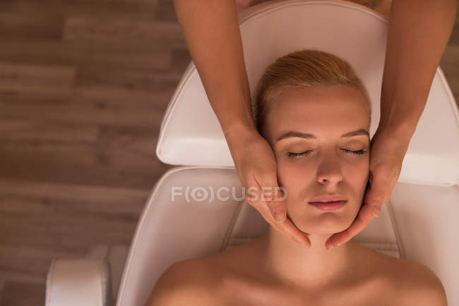 Косметолог дає масаж обличчя жінці-клієнту у вітальні — стокове фото