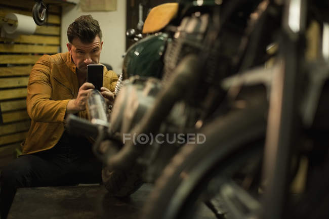 Механик фотографирует мотоцикл с мобильным телефоном в гараже — стоковое фото