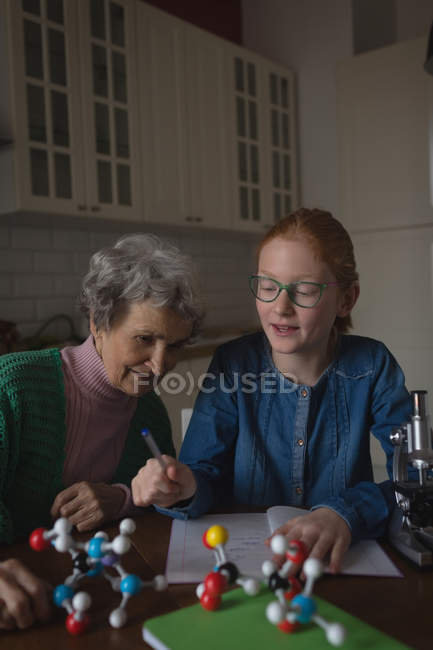 Бабуся допомагає онуці з домашнім завданням на кухні вдома — стокове фото
