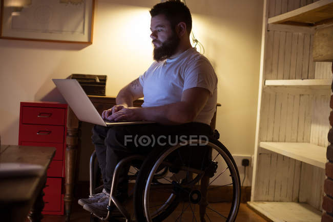 Hombre joven discapacitado usando el ordenador portátil en casa - foto de stock