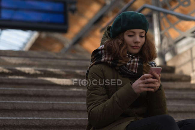 Женщина в зимней одежде с помощью мобильного телефона на лестнице — стоковое фото
