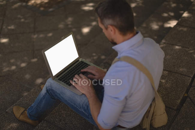 Вид сзади человека с помощью ноутбука на ступеньках — стоковое фото