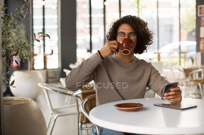 Hombre joven tomando café mientras usa el teléfono móvil en el restaurante - foto de stock