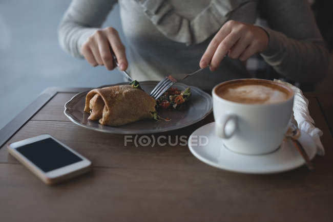 Mid section of woman having food with spoon and fork in cafe — Stock Photo