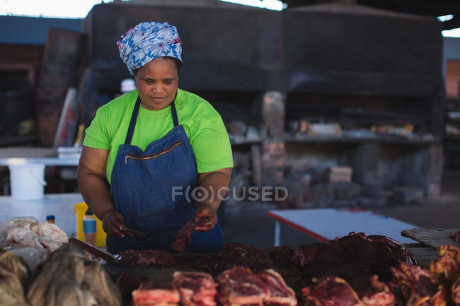 Female butcher cutting meat at counter in butchery — Stock Photo