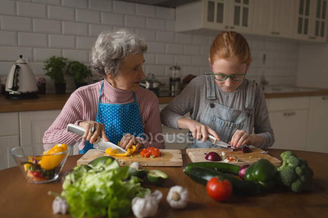 Бабушка и внучка режут овощи на кухне дома — стоковое фото