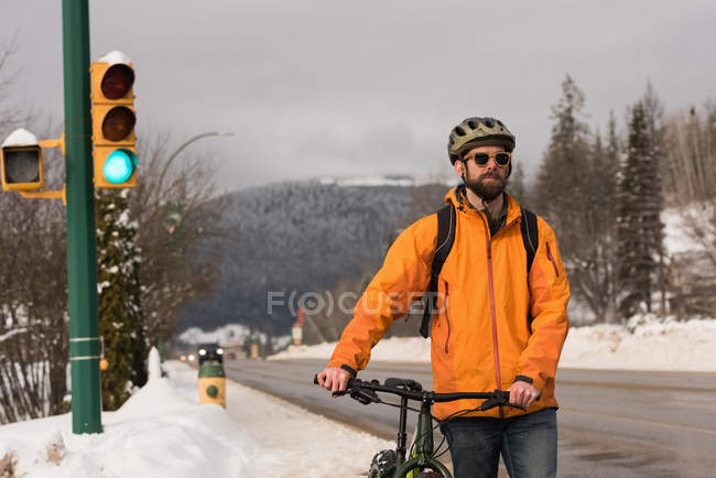 Man walking with his cycle on sidewalk during winter — Stock Photo