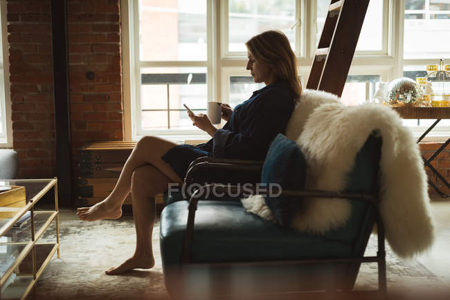Жінка, що використання мобільного телефону під час вдома за кавою — стокове фото
