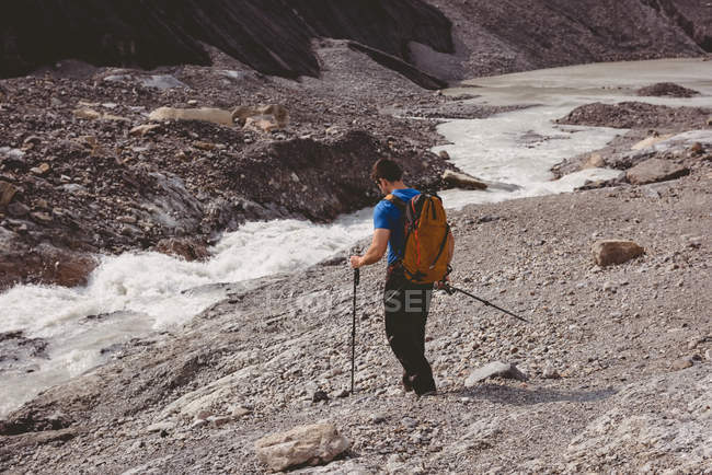 Caminhante masculino com mochila andando perto do rio em um dia ensolarado — Fotografia de Stock