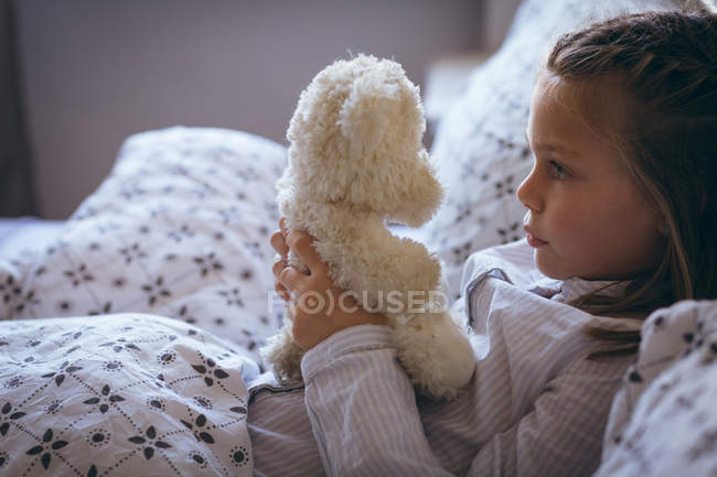Ragazza che gioca con orsacchiotto sul letto in camera da letto — Foto stock