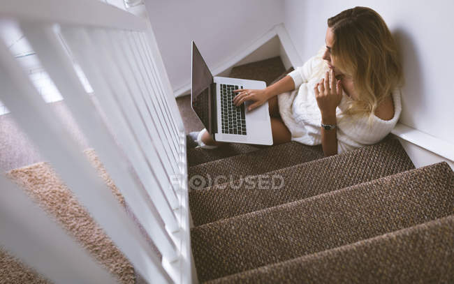Frau benutzt Laptop, während sie zu Hause im Treppenhaus sitzt — Stockfoto