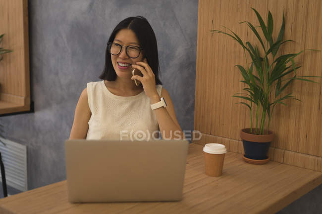 Беременная деловая женщина разговаривает по мобильному телефону за столом в офисе — стоковое фото