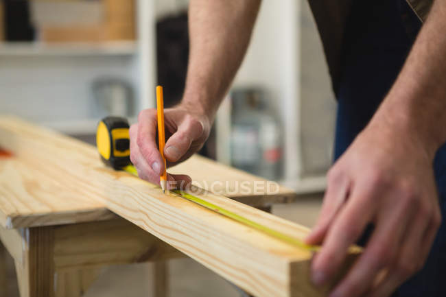 Section médiane du menuisier mâle mesurant et marquant le bois en atelier — Photo de stock