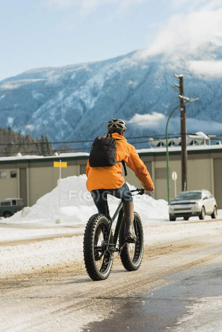 Вид сзади на человека, едущего на велосипеде по улице зимой — стоковое фото