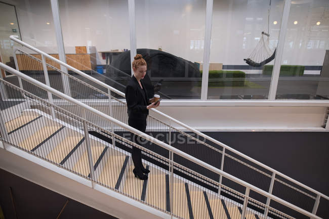 Женщина графический дизайнер с помощью мобильного телефона на эскалаторе в офисе — стоковое фото