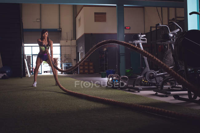 Adatta donna che fa esercizio di corda da battaglia in palestra — Foto stock