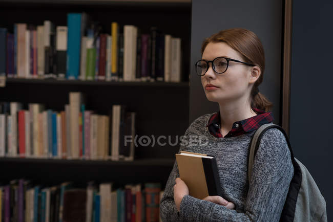 Thoughtful woman with book standing in the library — Stock Photo