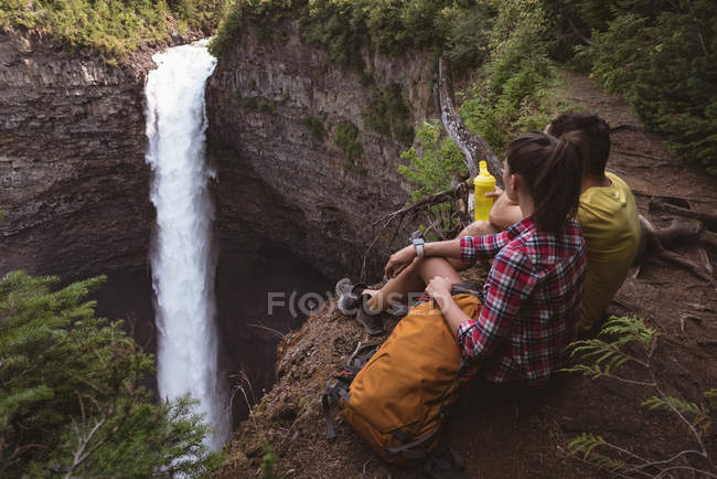 Casal sentado perto de cachoeira em um dia ensolarado — Fotografia de Stock
