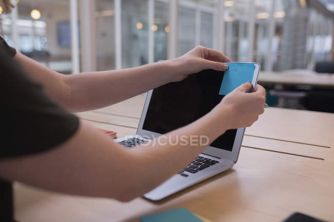 Female executive sticking sticky note on laptop in office — Stock Photo