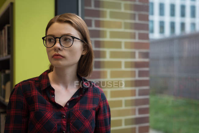 Nachdenkliche Frau steht in der Bibliothek — Stockfoto