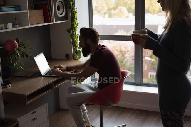 Man using laptop while woman holding coffee cups at home — Stock Photo