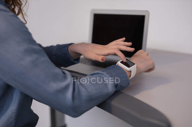 Mid section of female executive using smartwatch on treadmill in office — Stock Photo