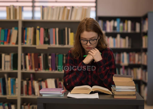 Mujer joven leyendo un libro en la biblioteca - foto de stock