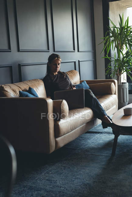 Businesswoman using laptop on a sofa in office — Stock Photo