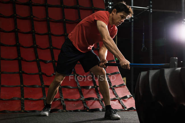 Hombre de fitness golpeando neumático rueda con martillo de trineo en el gimnasio - foto de stock