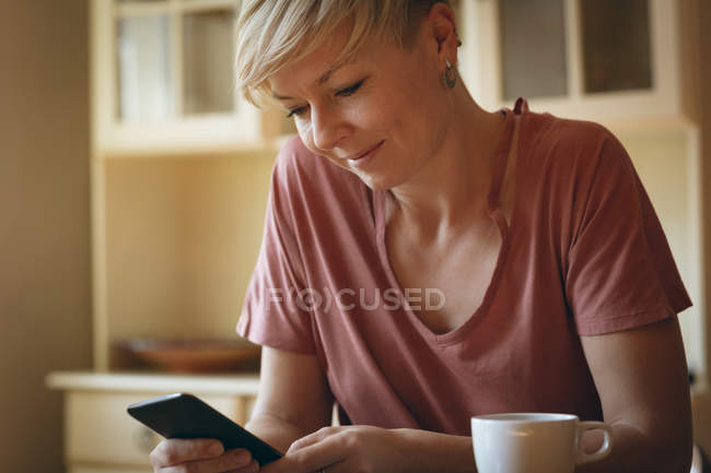 Femme souriante utilisant un téléphone portable à la maison — Photo de stock