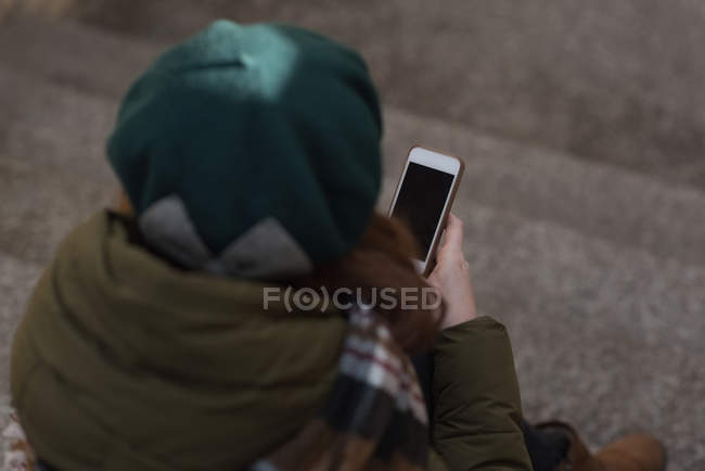Frau in Winterkleidung benutzt Handy im Treppenhaus — Stockfoto