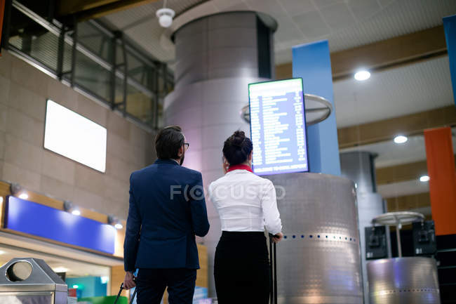 Homme d'affaires et femme regardant le tableau de départ à l'aéroport — Photo de stock