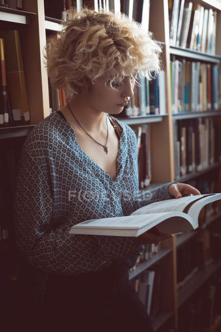Молода жінка читає книгу в бібліотеці — стокове фото