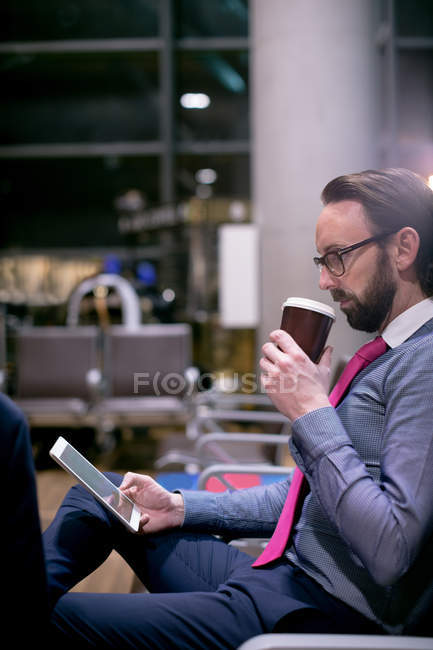 Бизнесмен, употребляющий цифровой планшет, пьет кофе в зале ожидания в аэропорту — стоковое фото