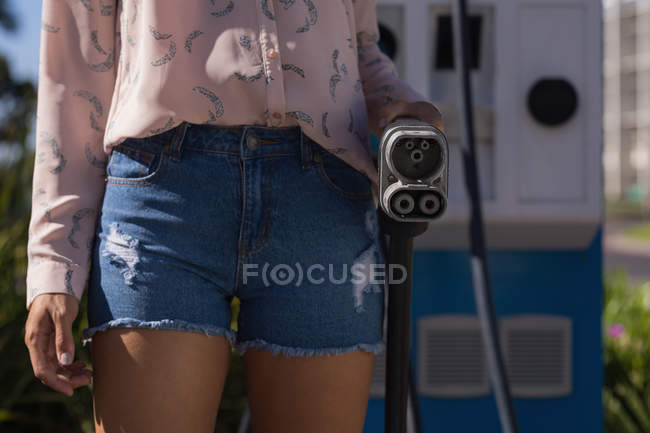 Mid section of woman holding a charging plug at charging station — Stock Photo