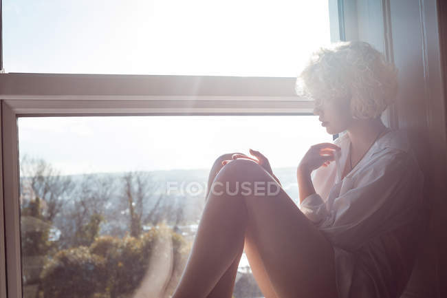 Mulher pensativa sentada perto da janela em casa — Fotografia de Stock
