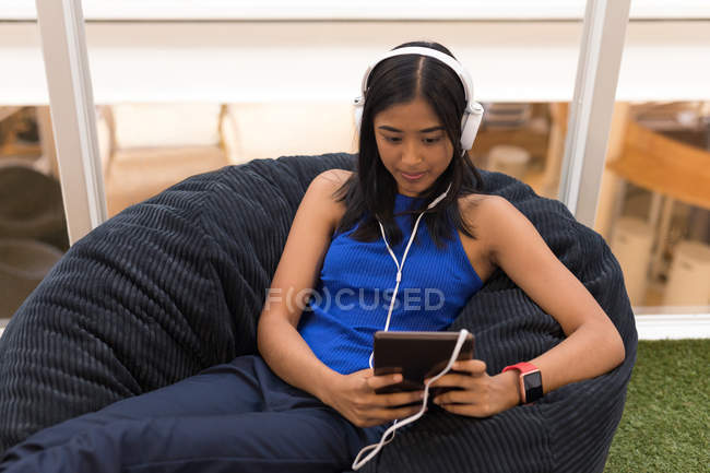Mulher usando tablet digital enquanto ouve música em fones de ouvido no escritório — Fotografia de Stock